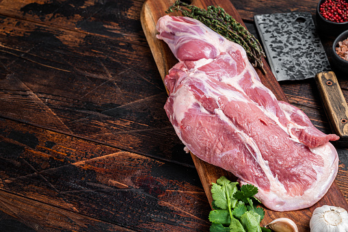 Raw lamb whole shoulder, fresh leg meat on a wooden board with spices. Wooden background. Top view. Copy space.