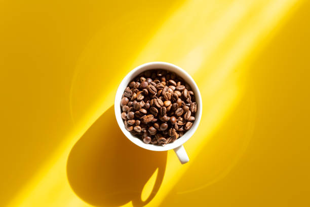Coffee beans in a white ceramic cup on a yellow background. Hard sun shadows. Top view Coffee beans in a white ceramic cup on a yellow background. Hard sun shadows. Top view - Image harsh shadows stock pictures, royalty-free photos & images