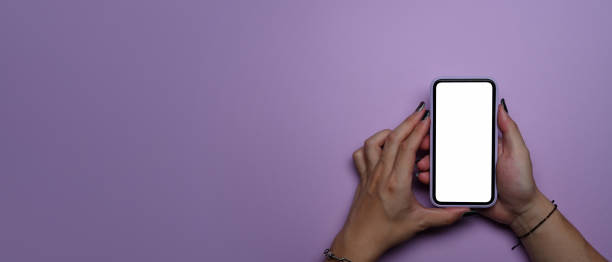 istock Young woman hands using smart phone with blank screen on purple background with copy space. Top view. 1389086567