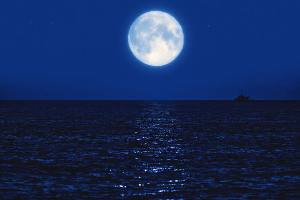 istock Full Moon rising above ocean horizon with boat silhouette. 1389093230