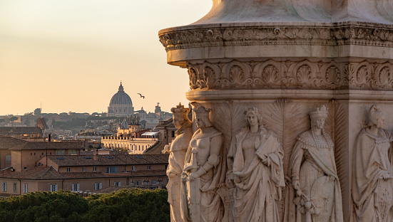 A picture of the base of the Equestrian Statue of Vittorio Emanuele II overlooking the St. Peter's Basilica at sunset.