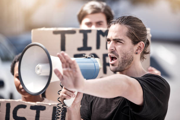 istock Shot of a young man yelling through a megaphone during a protest 1389094789