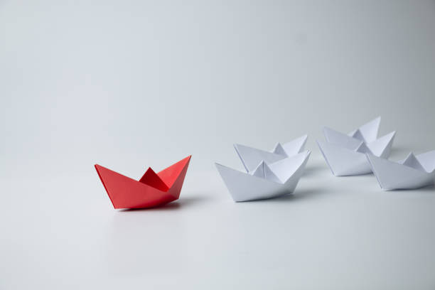 istock Red paper ship leading among white 1389095058