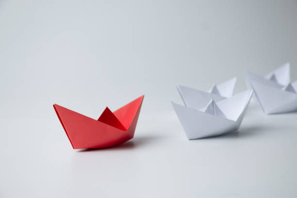 istock Red paper ship leading among white 1389095068