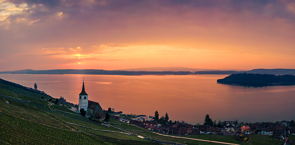 Panoramic view of the vineyards above the municipality of Ligerz, the church of Ligerz, Lake Biel and part of St. Peter's Island on the right. Sunrise with a partly cloudy sky. Morning mood near the city of Biel Bienne, canton Bern, Switzerland