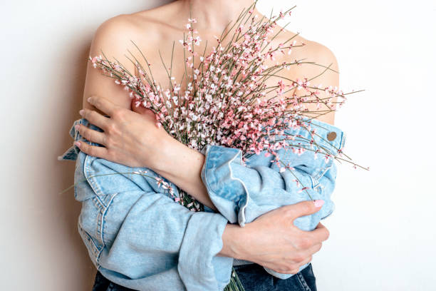 Young woman with bare shoulders holding a  pink genista flowers in her hands.Hands close-up.Spring,awakening of nature concept.Beauty and tenderness concept stock photo