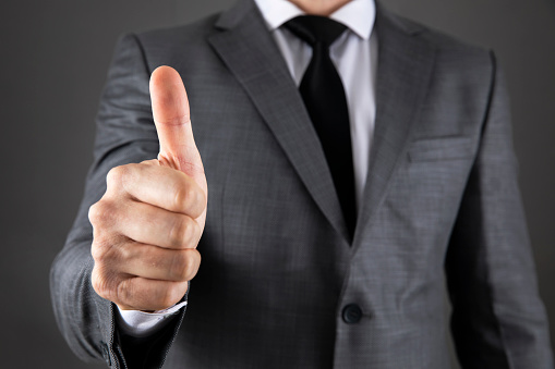 Business man shows thumb up sign gesture on grey background.