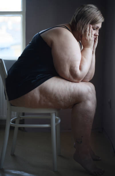 mujer solitaria deprimida sentada y mirando por la ventana de casa. - mature adult sadness overweight women fotografías e imágenes de stock