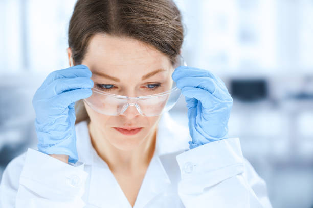흰색 실험실 코트를 입은 젊은 여성 과학자가 보호 안경을 조정합니다. - pcr device science research test tube 뉴스 사진 이미지