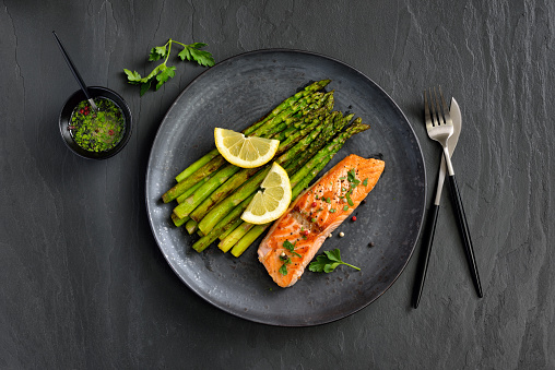 Fried salmon fillet with green asparagus, served with lemon vinaigrette on dark slate background