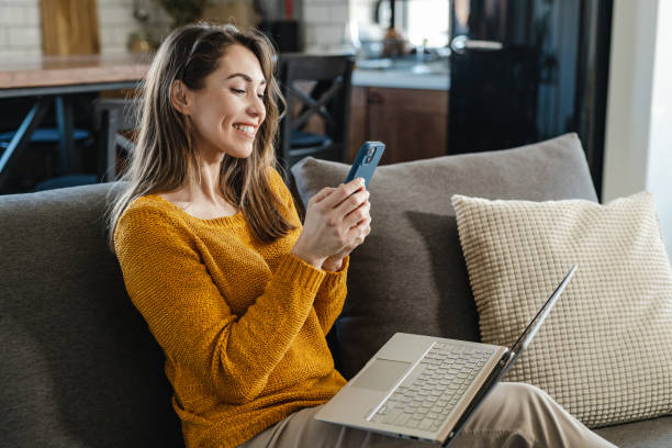 istock Beautiful woman using mobile phone and laptop at home 1389116399