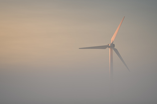 Wind turbine in the morning mist. Minimalistic landscape. Green energy theme