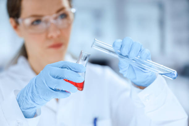 실험실 코트와 보호 장갑을 착용한 젊은 백인 여성 연구원이 실험실 플라스크에 색깔의 액체를 혼합합니다. - pcr device science research test tube 뉴스 사진 이미지