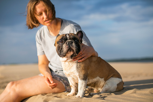 Young woman with her french bulldog sitting at the beach