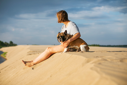 Young woman with her french bulldog sitting at the beach