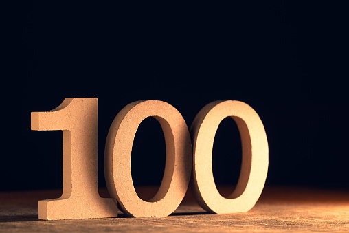 One hundred number set by cut wood figure on dark background with spot light on it, 100 or 100th concept