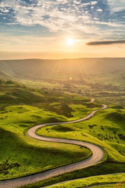 Long Winding Rural Road Leading To Beautiful Sunset. Peak District, UK. Winding country road leading to Edale in the English Peak District with beautiful golden light shining through valley. winding road stock pictures, royalty-free photos & images