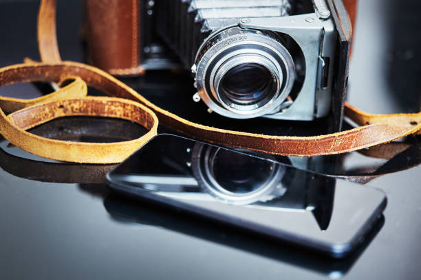 istock Eras of photography: Modern cellphone with antique folding bellows rangefinder camera, with weathered leather strap 1389126197