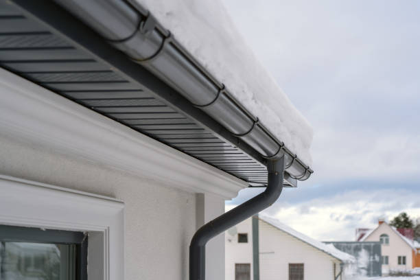 Corner of house with new roof made of gray metal tiles and gutter covered with thick layer of snow in winter. Metal Downpipe system, Guttering System, External downpipes and drainage pipes stock photo