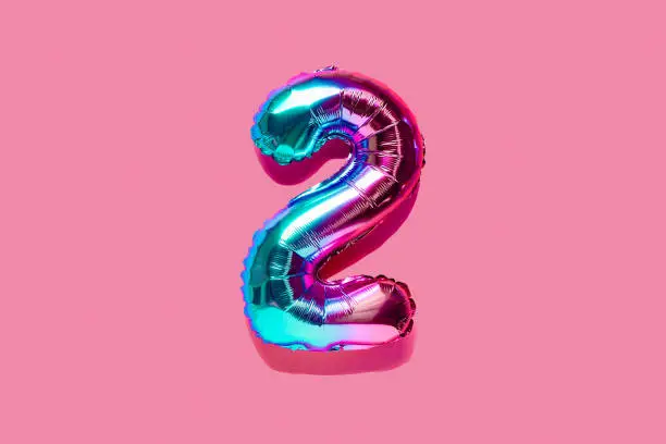 Rainbow foil balloon number, digit two . Top view. Colored numeral on pink background.