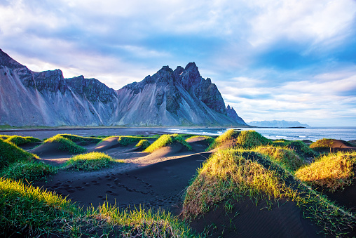 Scenic landscape with most beautiful mountains Vestrahorn on the Stokksnes peninsula and cozy lagoon with green grass on the sand dunes at sunset in Iceland. Exotic countries. Amazing places.