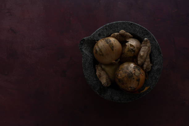 Onions and ginger in a mortar bowl, placed on a coloured background, with empty space for text to the left. Still life food photography