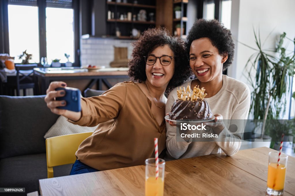 Lesbian Latin American woman posing with her partner while holding a birthday cake Portrait of two lesbian women taking a selfie with chocolate birthday cake. They are using a smart phone. Birthday Stock Photo