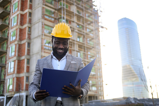 Mid adult engineer or architect on a construction site in a city, reading paperwork. About 30 years old, African male.