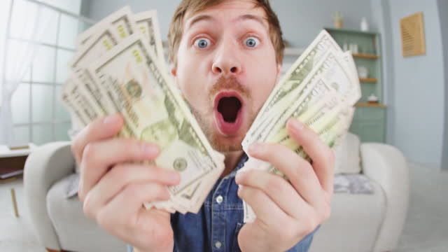 Portrait of excited young man holding bunch of money banknotes and celebrating