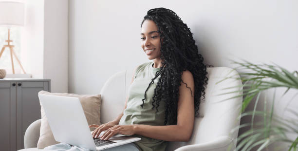 istock Young woman on couch using laptop computer, relaxing at home 1389144972