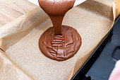 Pouring a liquid thick mass of cocoa dough onto a baking sheet lined with baking paper.