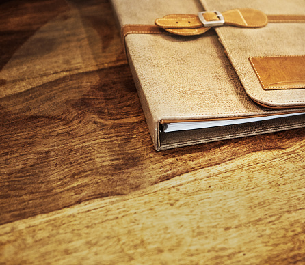 On a desk or table with rich wood grain, a high-quality leather folder containing paperwork.