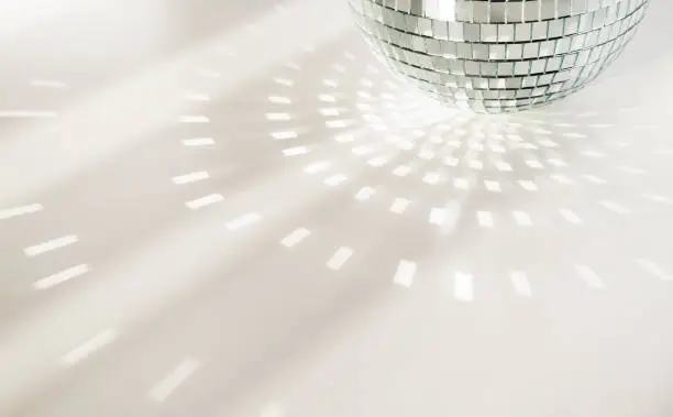 Photo of Disco ball on a white background with shadows and casts rays of bright light. Glare and light reflection