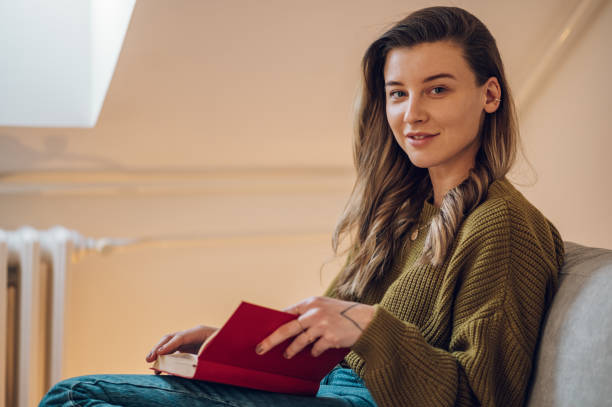 istock Woman reading a book while sitting on the couch at home 1389147283