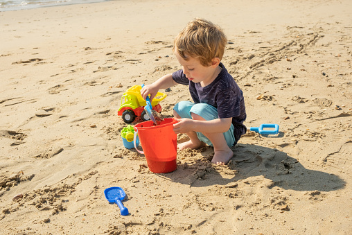 Small boy aged 2.5 years building sand castles on the beach, England, UK.