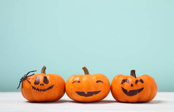 istock Pumpkins with scary faces on light turquoise background, space for text. Halloween decor 1389148955