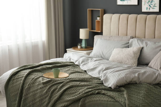 istock Comfortable bed with knitted green plaid in stylish room interior 1389149636