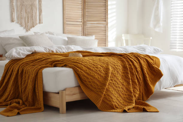 istock Comfortable bed with warm knitted plaid in stylish room interior 1389149797