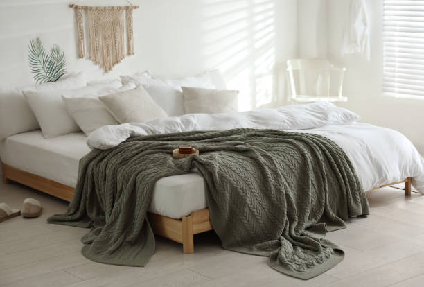 istock Comfortable bed with warm knitted plaid in stylish room interior 1389149850