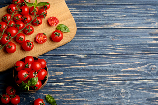 Fresh ripe cherry tomatoes and basil on blue wooden table, flat lay. Space for text