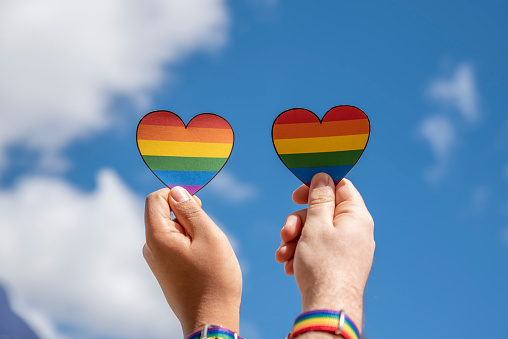 two hands holding hearts with the lgbt rainbow flag on blue sky