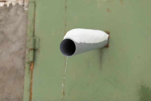 Pipe in wall. Draining water from sewer. Water conduit on street. Plastic pipe is covered with snow.