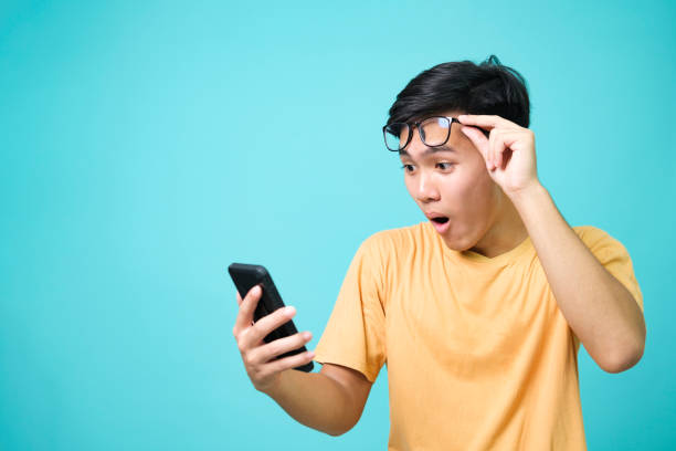 young asian man with surprised facial expression hold smartphone in his hands. - great discounts imagens e fotografias de stock