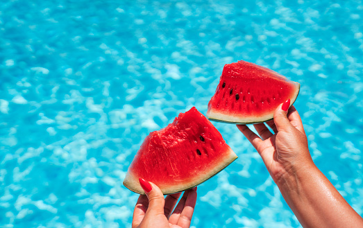 Two slices of watermelon in hands by the pool on a summer day. High quality photo