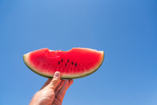 slice of watermelon in a female hand against a blue sky High quality photo