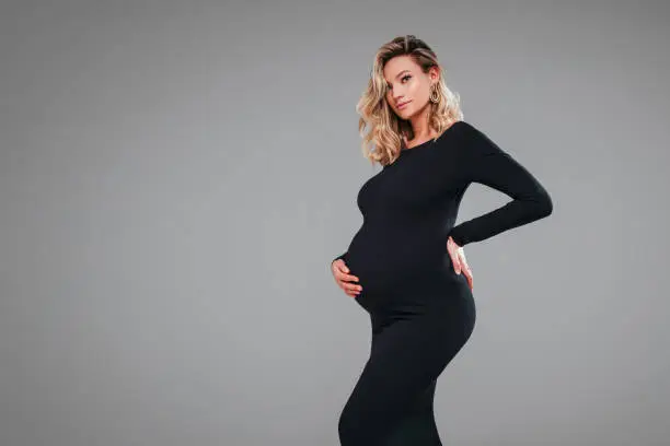 Photo of Pregnant beautiful Woman in black maxi dress touching her belly. Beauty young mother portrait.