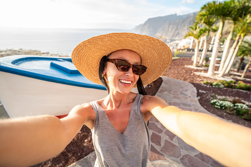 Happy woman in summer hat smiling to the camera, taking selfie on Tenerife, Los Gigantes . Canary islands. View point. Tourism. Tourist. Travel.