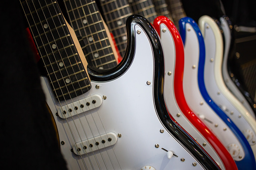 Row of electric guitars In a music instruments shop. Parts of guitar, body, black, white, blue and red