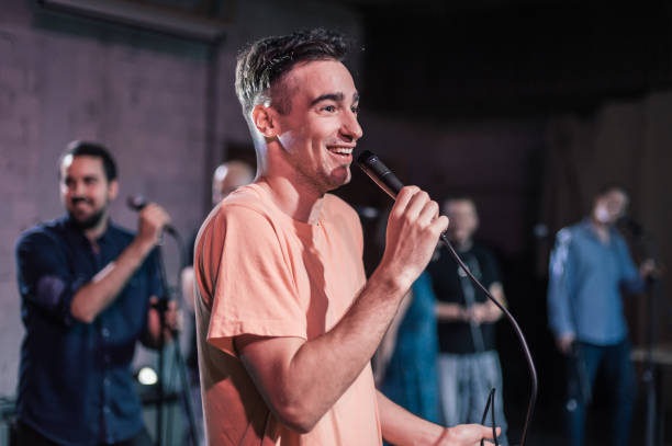 lächelnder und witziger stand-up-schauspieler comedian auf der bühne, spricht und singt - darstellender künstler stock-fotos und bilder