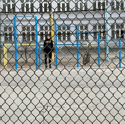 Kyiv Ukraine-March 2022: The guy is standing on the sports ground. View through the metal mesh fence.